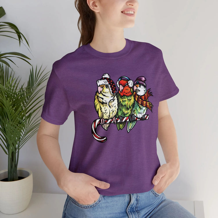 Woman wearing purple t-shirt with graphic of 3 lovebirds in winter hats & scarves.